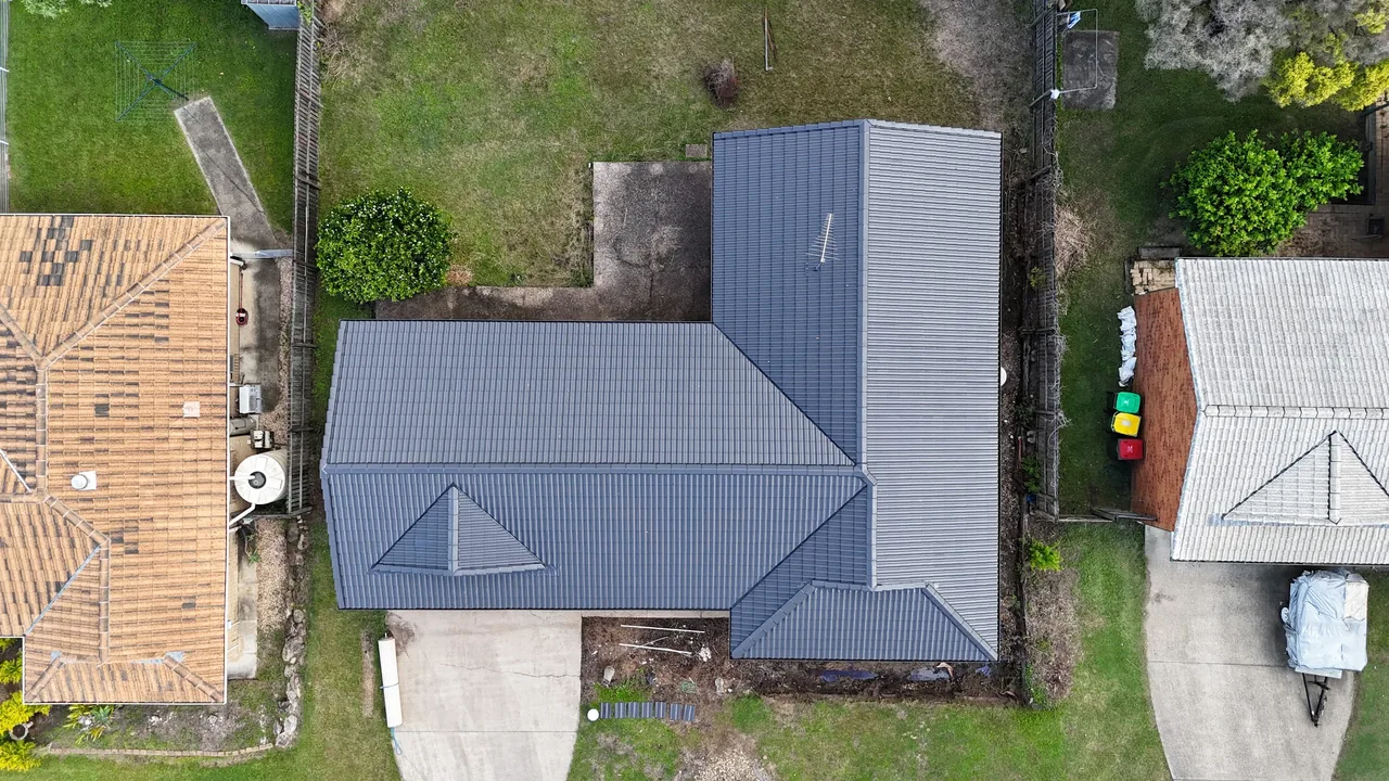 Freshly recoated charcoal roof beside an un-restored terracotta roof, aerial view